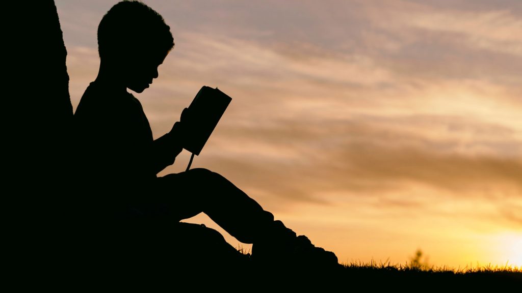 Silhouette of a boy reading at sunset.